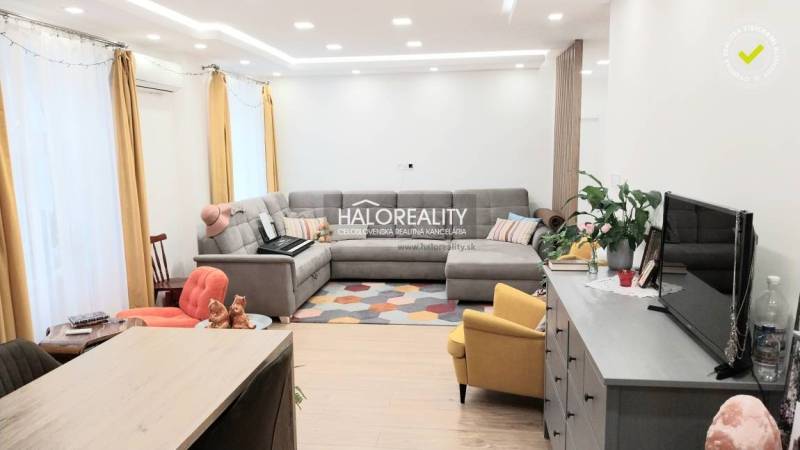 Predaj, trojizbový byt Komárno - Obývacia izba v 3-izbovom byte s podlahou s dreveným dekorom, sivou sedačkou a žltým kreslom.