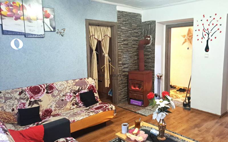 HD reality, Predaj 2-izbového bytu, Veľký Krtíš - Obývacia izba v 2-izbovom byte s kachľovou pecou a podlahou s dreveným dekorom.