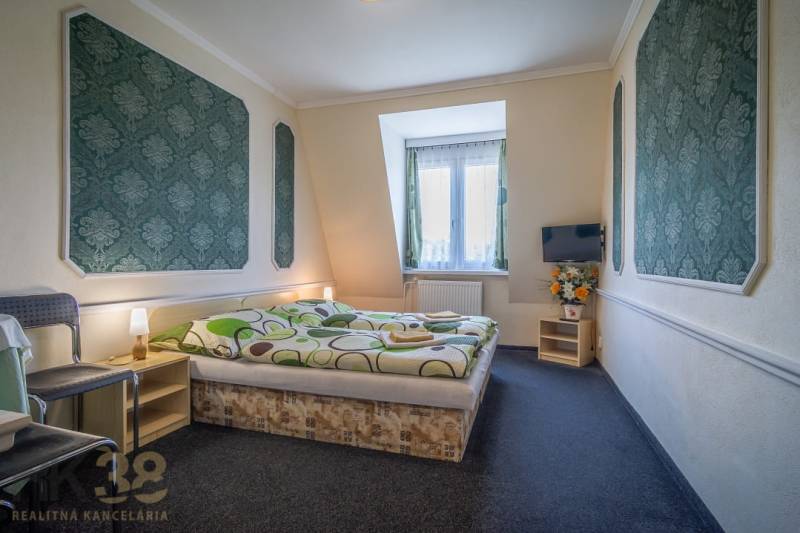 Predaj nehnuteľnosti v mestskej časti Poprad-Veľká - Izba s manželskou posteľou, kobercovou podlahou, televízorom, stoličkou a dekoráciami v Hoteloch a penziónoch.
