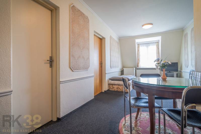 Predaj nehnuteľnosti v mestskej časti Poprad-Veľká - Interiér hotela a penziónu s okrúhlym stolom, koberec, TV a ozdobné steny.