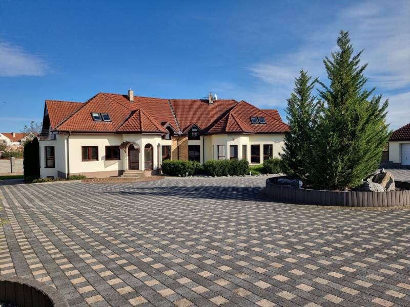 EXKLUZÍVNA VILA - NITRA - PREDAJ - Rodinný dom na Dolnočermánskej ulici v Nitre s veľkou dlaždenou plochou a stromami.