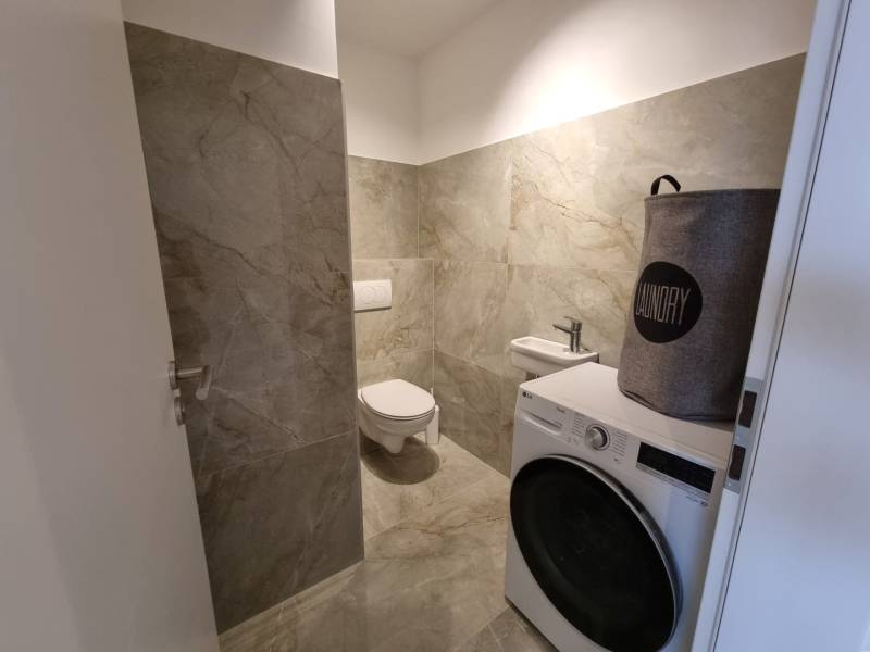 PRENÁJOM - 3 izbový byt Nitra – RIVIERA NITRA, Piesková ulica - Kúpeľňa so sivými dlaždicami, práčkou a košom na prádlo v 3-izbovom byte.