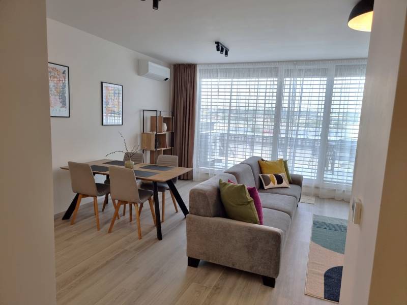 PRENÁJOM - 3 izbový byt Nitra – RIVIERA NITRA, Piesková ulica - Obývacia izba v 3-izbovom byte obsahuje sedačku, jedálenský stôl a veľké okno.