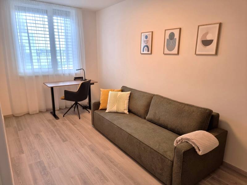 PRENÁJOM - 3 izbový byt Nitra – RIVIERA NITRA, Piesková ulica - Izba v 3-izbovom byte s gaučom, stolíkom, stoličkou a modernými obrazmi na stene.