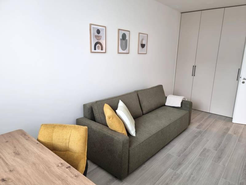 PRENÁJOM - 3 izbový byt Nitra – RIVIERA NITRA, Piesková ulica - Sivá sedačka s vankúšmi a drevený stôl v 3-izbovom byte, biele steny, skrine.