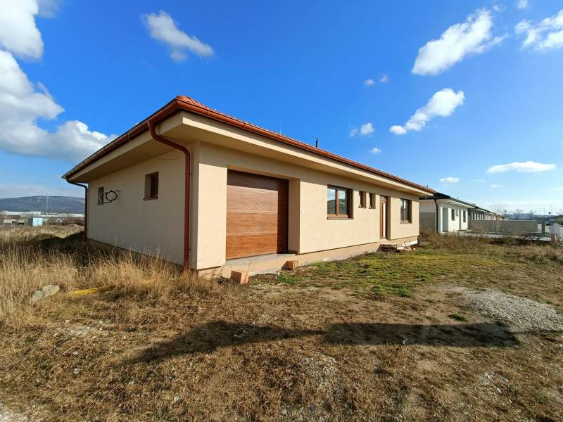 PREDAJ - 4 izbový holodom s veľkou garážou , Lužianky, Smreková ulica - Jednopodlažný rodinný dom s červenou strechou, obklopený prírodou a trávnatými plochami.