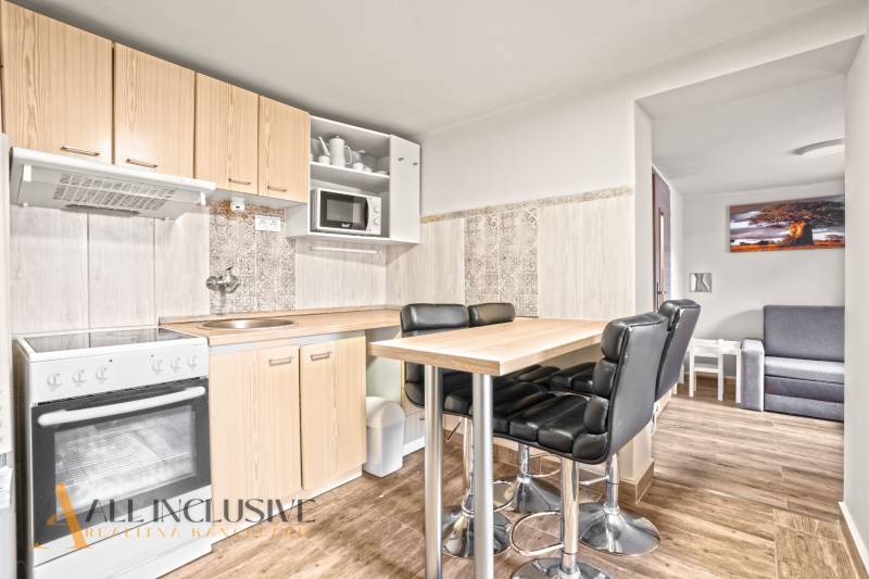 NA PREDAJ 5+2 IZBOVÝ RD PRI KÚPALISKU, DUNAJSKÁ STREDA - Kuchyňa v rodinnom dome s barovým stolom, čiernymi stoličkami a podlahou s dreveným dekorom.