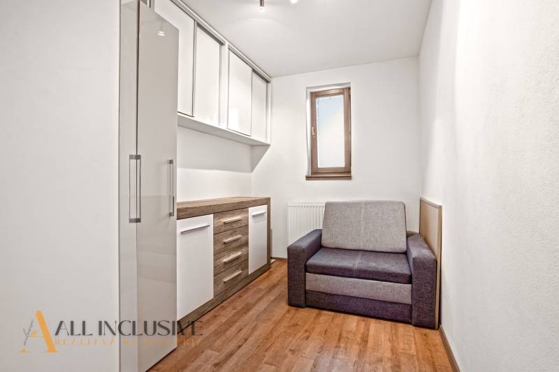 NA PREDAJ 5+2 IZBOVÝ RD PRI KÚPALISKU, DUNAJSKÁ STREDA - Izba v rodinnom dome s podlahou s dreveným dekorom, sivou sedačkou a úložnými skrinkami.