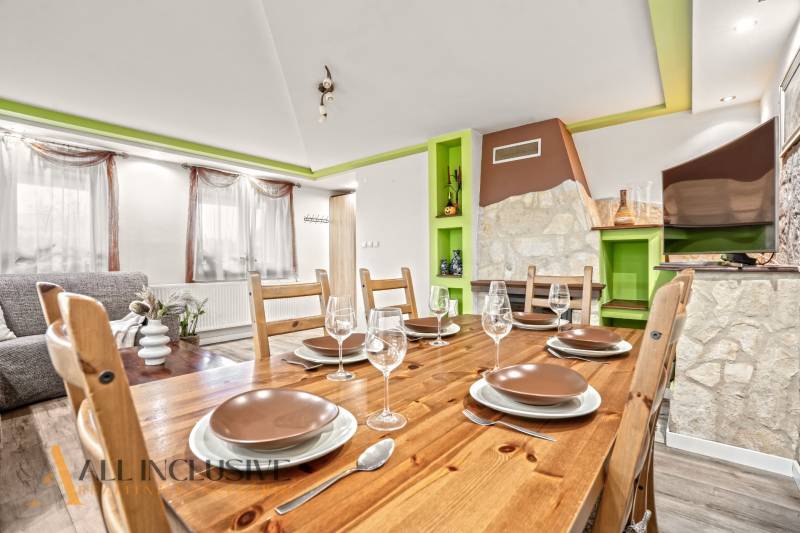 NA PREDAJ 5+2 IZBOVÝ RD PRI KÚPALISKU, DUNAJSKÁ STREDA - Jedáleň v rodinnom dome s dreveným stolom, pohármi a dekoratívnym kozubom.