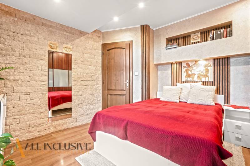 NA PREDAJ 5+2 IZBOVÝ RD PRI KÚPALISKU, DUNAJSKÁ STREDA - Spálňa v rodinnom dome s postelí, kamennými detailmi a podlahou s dreveným dekorom.