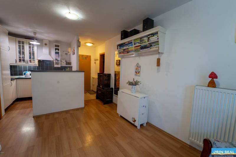 Na predaj útulný 2 izbový byt so zahradkou Svätý Jur 165.000,- Eur - Interiér 2-izbového bytu s kuchyňou, police s knihami, podlaha s dreveným dekorom.