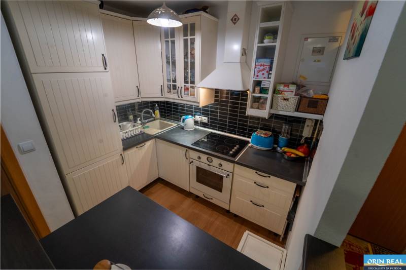 Na predaj útulný 2 izbový byt so zahradkou Svätý Jur 165.000,- Eur - Kuchyňa v 2-izbovom byte s svetlými skrinkami a podlahou s dreveným dekorom.