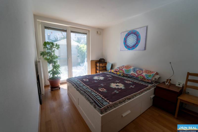 Na predaj útulný 2 izbový byt so zahradkou Svätý Jur 165.000,- Eur - Spálňa v 2-izbovom byte s posteľou, rastlinou a podlahou s dreveným dekorom.