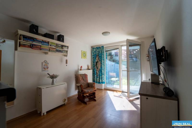 Na predaj útulný 2 izbový byt so zahradkou Svätý Jur 165.000,- Eur - Obývací priestor v 2-izbovom byte s podlahou s dreveným dekorom a prístupom na terasu.