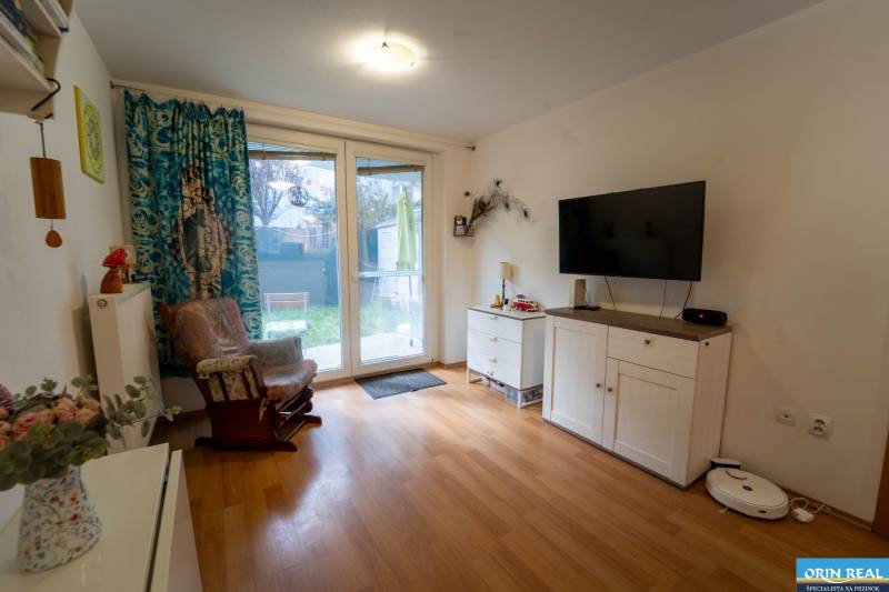 Na predaj útulný 2 izbový byt so zahradkou Svätý Jur 165.000,- Eur - Obývacia izba v 2-izbovom byte s podlahou s dreveným dekorom, televízorom a kreslom.