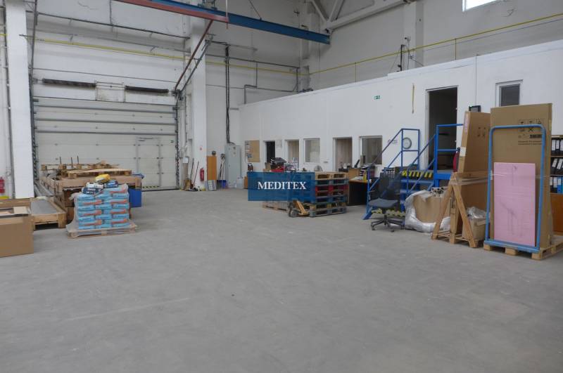 Sklad na prenájom o celkovej ploche 1015 m2 - Interiér skladu s vysokými stropmi, skladacími bránami a rôznym tovarom na paletách.