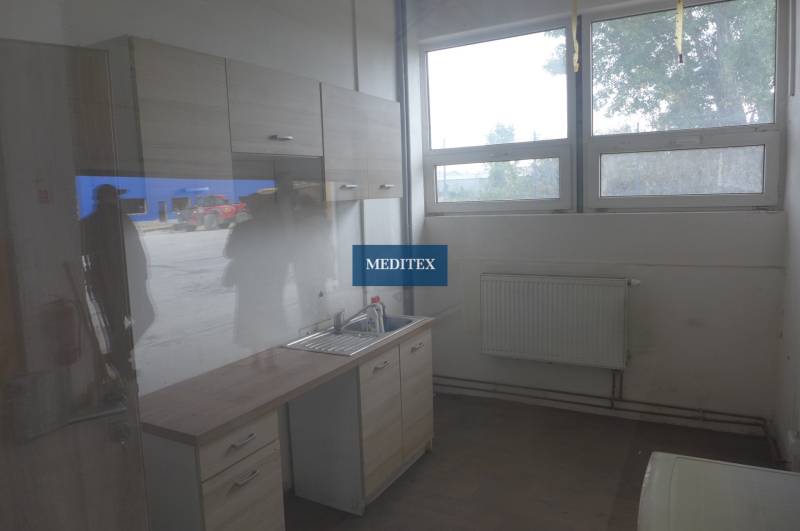 Sklad na prenájom o celkovej ploche 1015 m2 - Kuchynská časť so skrinkami, umývadlom a podlahou s dreveným dekorom v prostredí skladov a hál.