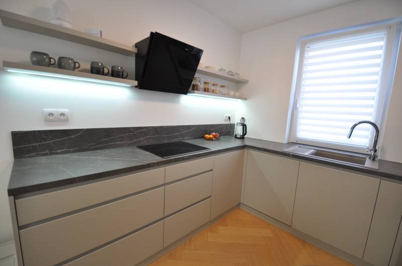 Perla v mori priemernosti - 4i prémiový RD Miloslavov - Kuchyňa v rodinnom dome s tmavou pracovnou doskou a podlahou s dreveným dekorom.