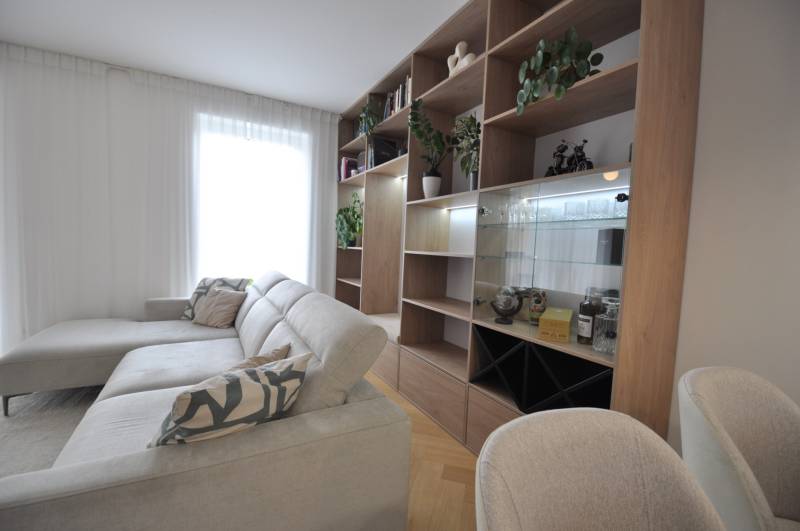 Perla v mori priemernosti - 4i prémiový RD Miloslavov - Obývacia izba v rodinnom dome s bielym gaučom, drevenou knižnicou a rastlinami.