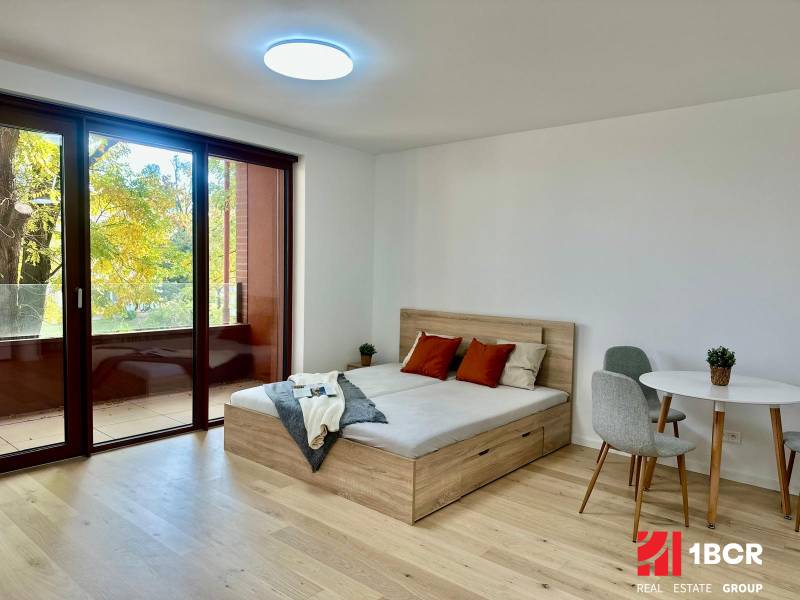 PRIESTRANNÝ 1-IZB. BYT S LOGGIOU V IKONICKOM PROJEKTE ZWIRN III - 1-izbový byt s posteľou, stolom a podlahou s dreveným dekorom.