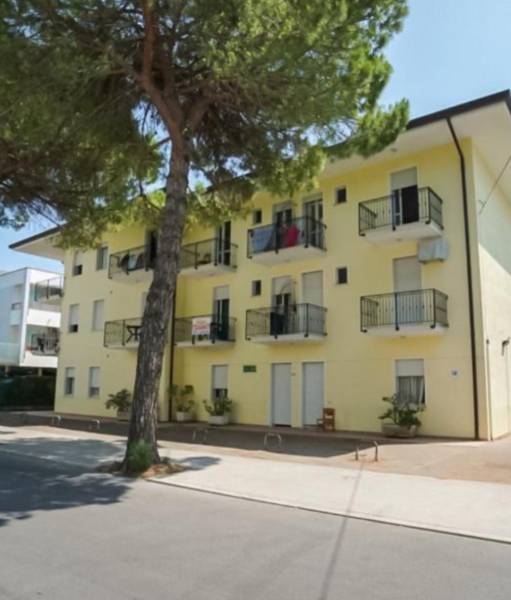 POLYFUNKČŇÁ BUDOVA PRIEVIDZA - Žltá budova s balkónmi a stromom v Prievidzi, vhodná pre hotely a penzióny.