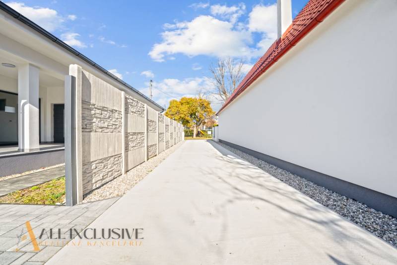 NA PREDAJ 4-IZB.BUNGALOV S DVOJGARÁŽOU,ORECHOVÁ POTôŇ - Úzka príjazdová cesta medzi rodinnými domami v Orechovej Potôni, lemovaná múrom a stromami.