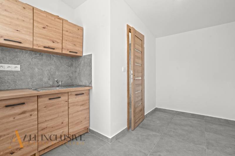 NA PREDAJ 4-IZB.BUNGALOV S DVOJGARÁŽOU,ORECHOVÁ POTôŇ - Kuchynská linka s drevodekorom a sivým obkladom v rodinnom dome, dlaždicová podlaha.