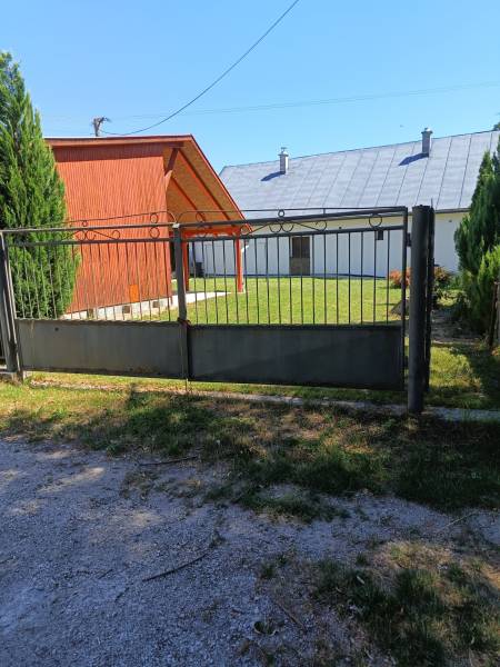 TUŽINA okres Prievidza - CHATA s terasou a garážou  - Brána a drevená chata v Tužine, obklopené trávnikom a ihličnanmi.