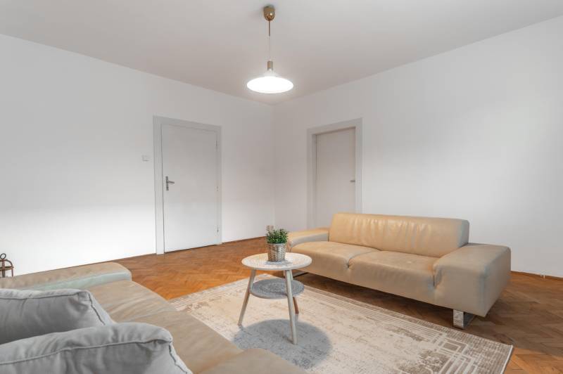 REZERVOVANÉ I Predaj charizmatického bytu Pavlovova ulica - Obývacia izba v 3-izbovom byte so svetlými sedačkami a podlahou s dreveným dekorom.