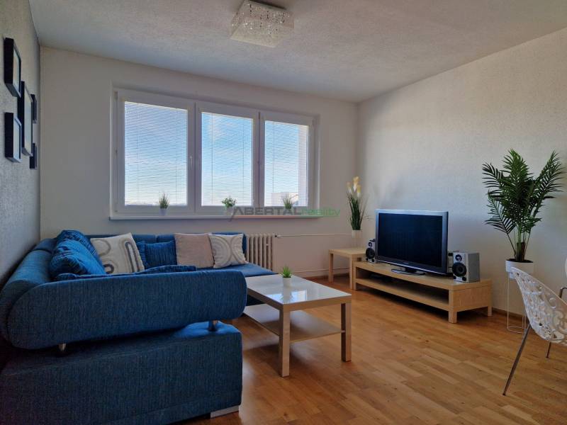 PRENÁJOM zariadený 3-izb byt, Pribišova, Bratislava - Obývačka v 3-izbovom byte s modrou pohovkou, televíziou a podlahou s dreveným dekorom.