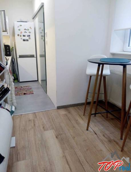 PRENÁJOM - 1,5 izbový byt Košice - Staré mesto - Kuchyňa v 1-izbovom byte s podlahou s dreveným dekorom, vysoký stolík a stoličky.