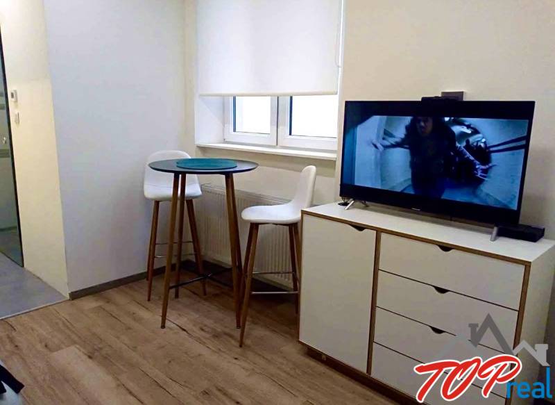 PRENÁJOM - 1,5 izbový byt Košice - Staré mesto - Interiér 1-izbového bytu s televíziou, barovým stolíkom a podlahou s dreveným dekorom.