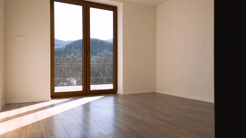 Predaj novostavba rodinného domu   Nová Baňa - Priestranná izba s veľkými oknami a podlahou s dreveným dekorom.