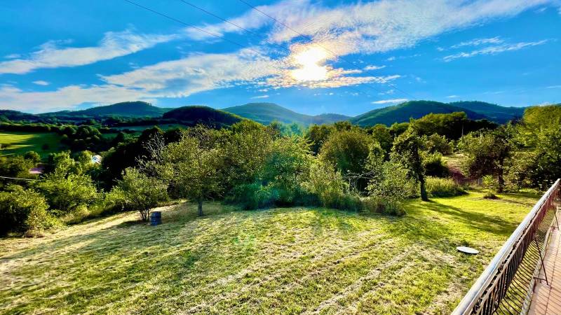 Predaj novostavba rodinného domu   Nová Baňa - Slnkom osvietená záhrada rodinného domu v Novej Bani s výhľadom na kopce.