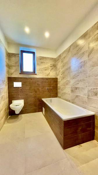 Predaj novostavba rodinného domu   Nová Baňa - Kúpeľňa s obkladmi v dekore dreva a dlažbou, vaňa a závesná toaleta.