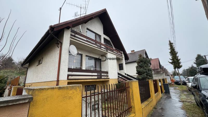 NA PREDAJ veľký rodinný dom v obci Pusté Úľany Sládkovičovo - Rodinný dom s balkónom, anténou a žltým plotom v pokojnej ulici.