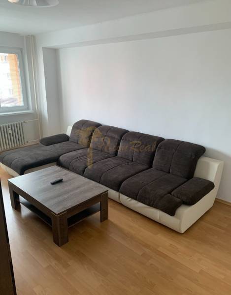 2-izb. byt, Nobelova ul., Nové Mesto, 2.p./7, balkón - Obývacia izba v 2-izbovom byte s tmavou pohovkou a podlahou s dreveným dekorom.