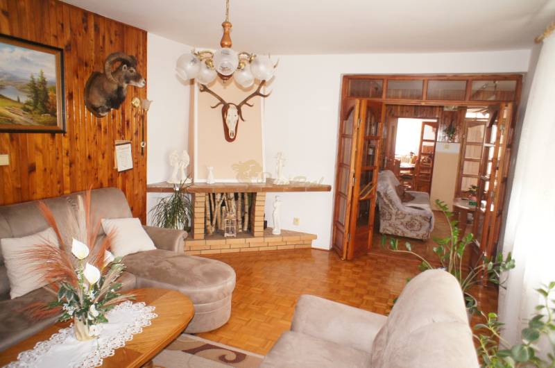 Rodinný dom v obci Čilížska Radváň s veľkým pozemkom - Rodinný dom s obývačkou, pohovkou, kobercami, poličkami a dekoráciou nad krbom.