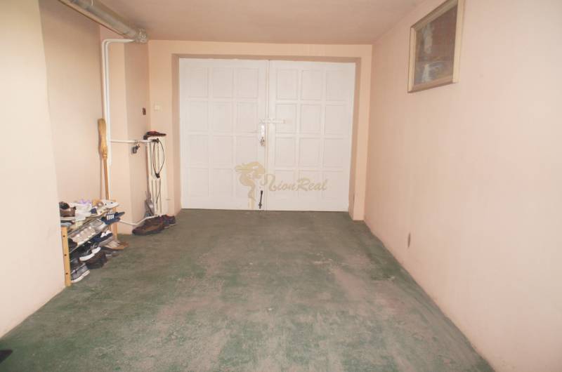 Rodinný dom v obci Čilížska Radváň s veľkým pozemkom - Garáž v rodinnom dome s bledými stenami, policou na topánky a bicyklom.