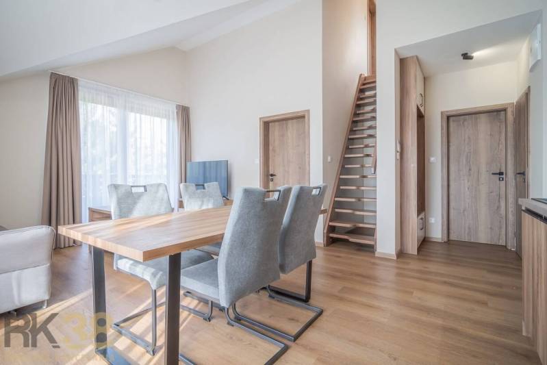 Lukratívne dvoj a štvorizbové byty v Tatranskej Lomnici na prenájom - Obývacia izba s jedálenským stolom a schodiskom v 2-izbovom byte, podlaha s dreveným dekorom.