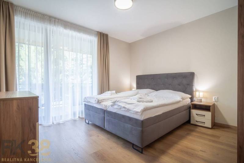 Lukratívne dvoj a štvorizbové byty v Tatranskej Lomnici na prenájom - Spálňa v 2-izbovom byte so svetlými závesmi a podlahou s dreveným dekorom.