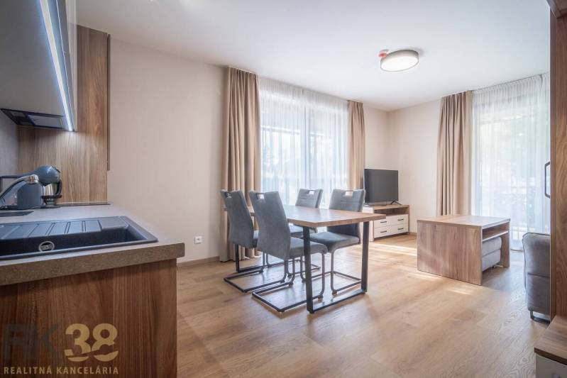 Lukratívne dvoj a štvorizbové byty v Tatranskej Lomnici na prenájom - Priestranný interiér 2-izbového bytu s podlahou s dreveným dekorom a jedálenským stolom.
