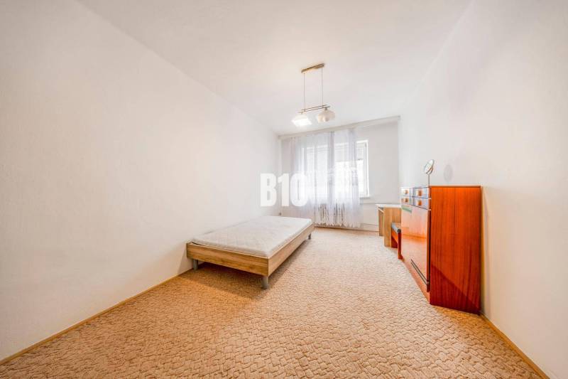 KRÍŽNA: VEĽKORYSÝ 4-IZBOVÝ BYT S RETRO ŠARMOM BLÍZKO CENTRA - Spálňa v 4-izbovom byte s posteľou, komodou a kobercom.