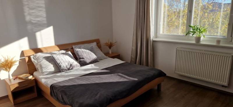 Novinka: Moderný  4-izb. mezonetový byt s balkónom a terasou. Muškát - Hlavná spálňa v 4-izbovom byte s podlahou s dreveným dekorom, jednoduchým nábytkom a doplnkami.