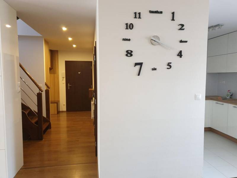 Novinka: Moderný  4-izb. mezonetový byt s balkónom a terasou. Muškát - Interiér 4-izbového bytu s hodinami na stene a podlahou s dreveným dekorom.