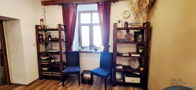 NA PRENÁJOM – odstúpenie vinotéky v srdci Starého Mesta s dušou vína - Knižnice s dekoráciami, stoličky a okno s bordovými závesmi v obchodnom priestore.