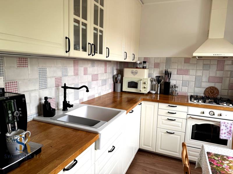 2-izbový byt v Seredi- bez rezervačnej zálohy - Kuchyňa 2-izbového bytu s bielymi skrinkami, drevenou pracovnou doskou a dekoratívnym obkladom.