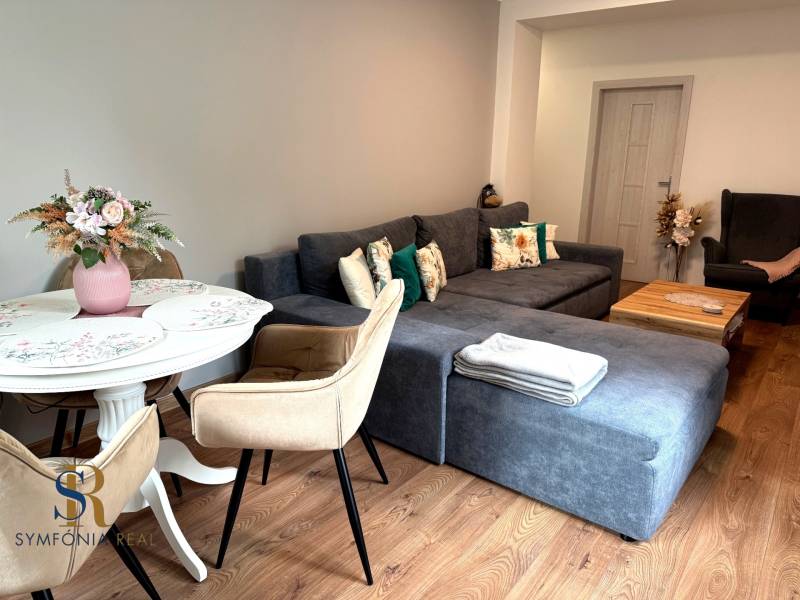 2-izbový byt v Seredi- bez rezervačnej zálohy - Obývacia izba s podlahou s dreveným dekorom, pohodlnou sedačkou a jedálenským stolom.