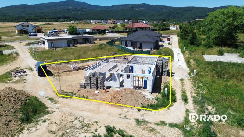 5-izbový dom 162m2 + pozemok 604m2 | Trenčianske Jastrabie - Stavba rodinného domu v Trenčianskom Jastrabí, obklopená vidieckou krajinou a susednými domami.