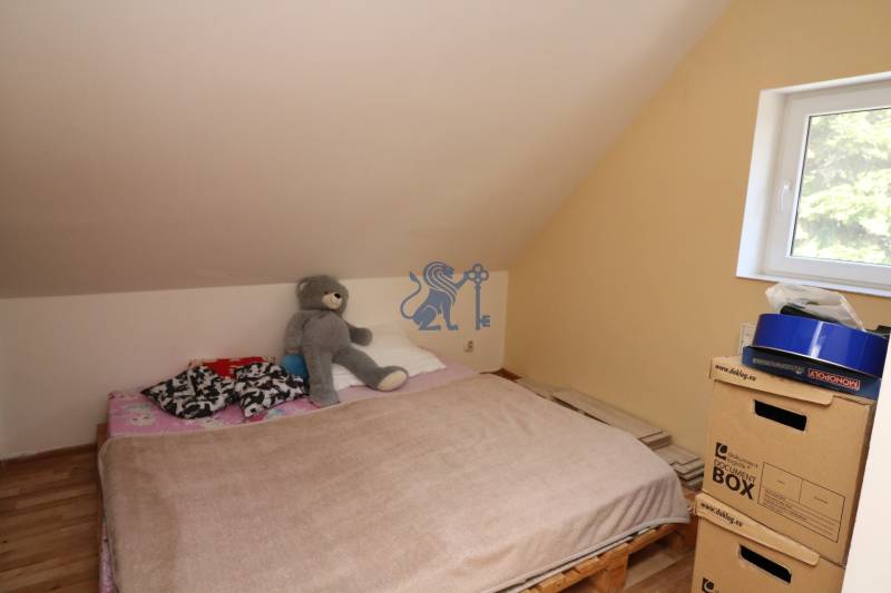 ZNÍŽENÁ cena - viacgeneračný  rodinný dom v Borinke  - Spálňa s paletovou posteľou, hnedou prikrývkou a mackom pri okne v podkroví.